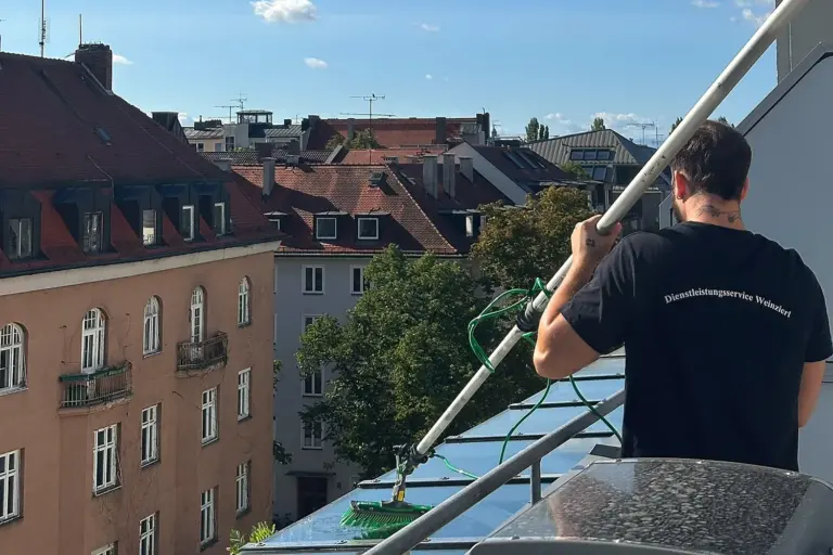 Michele Weinzierl reinigt ein Glasdach über den Dächern von München mit Teleskopstange